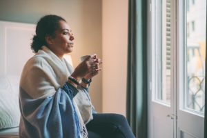 Woman wearing a blanket and drinking hot tea looking out of the window