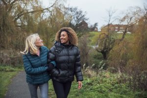 A senior caucasian woman and her mixed race daughter wearing casual winter clothing and walking through a local park.