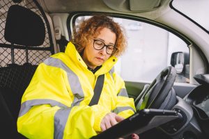 Focused delivery woman worker reviewing information on a tablet while seated in a delivery van.